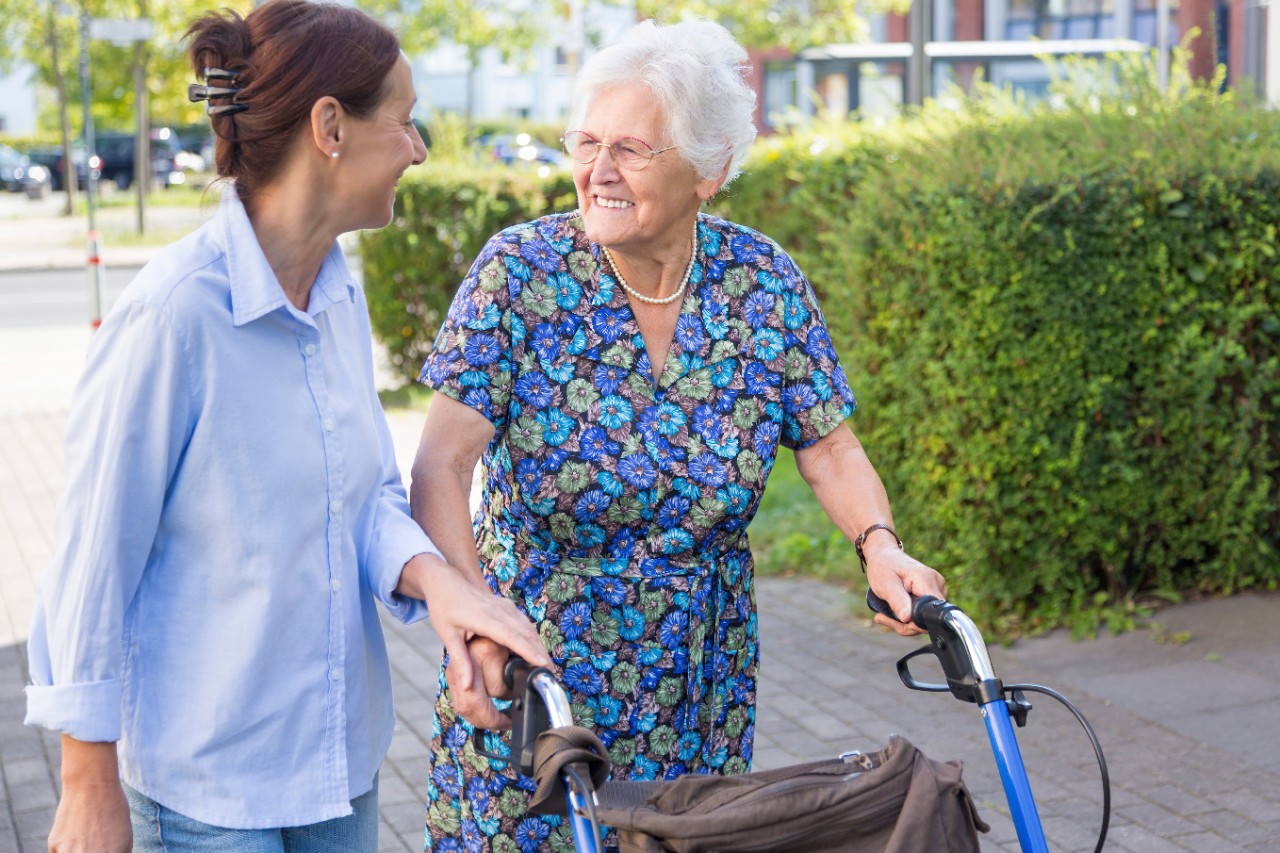 Mevrouw met een rollator wordt geholpen door een zorgverlener