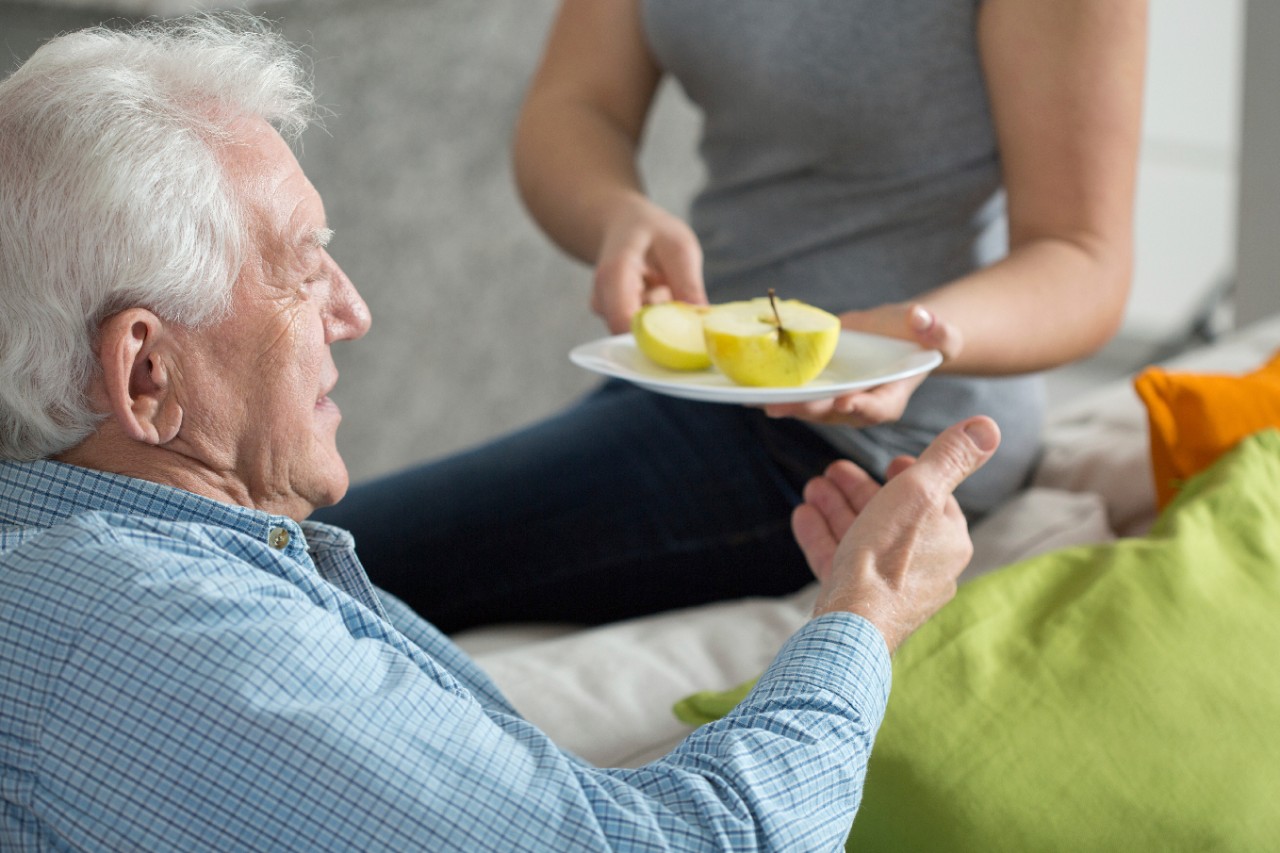 Mantelzorger reikt een patiënt een bord met partjes appel aan