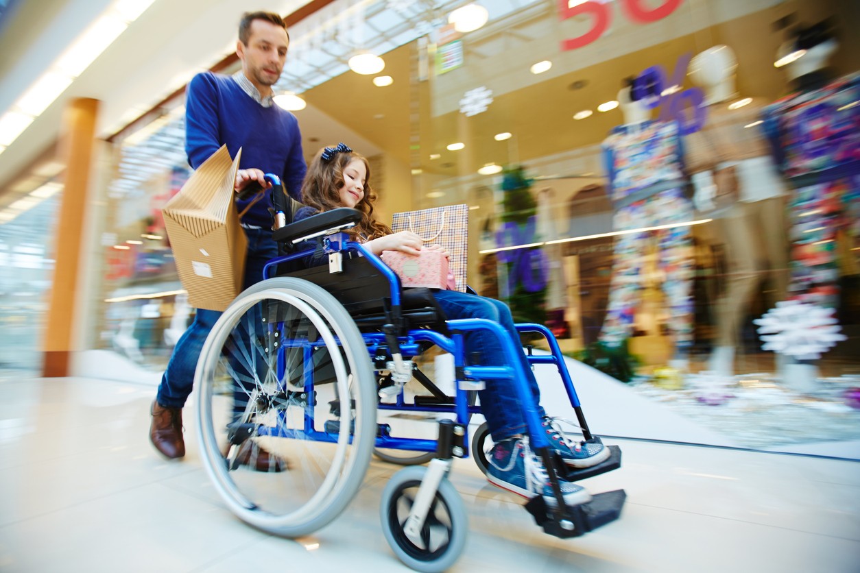 Rolstoel met kind wordt voortgeduwd door een winkelcentrum