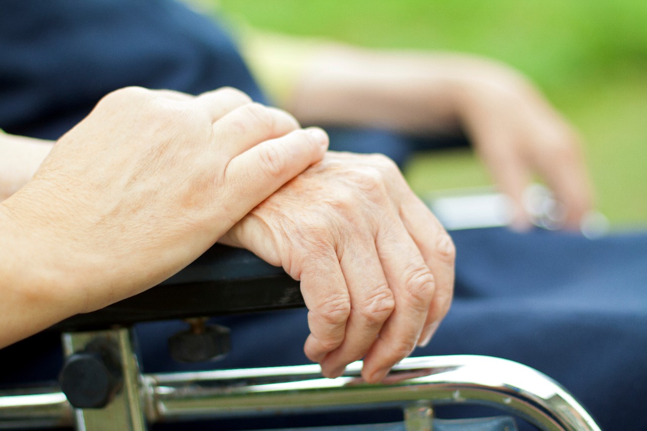 Mantelzorger legt hand op die van een Alzheimer-patiënt in een rolstoel