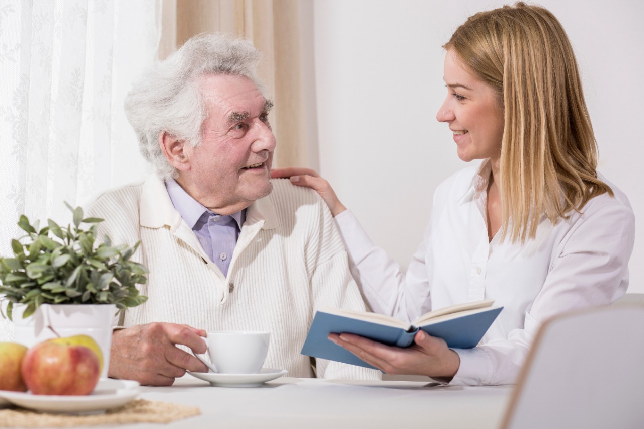 Senior in zijn seniorenwoning kijkt naar een dame met een boek